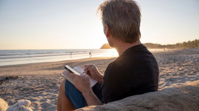 MP 398 Email Image 1 man sitting on a beach writing in journal