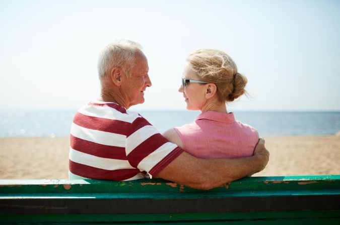 old couple sitting on a bench at the beach